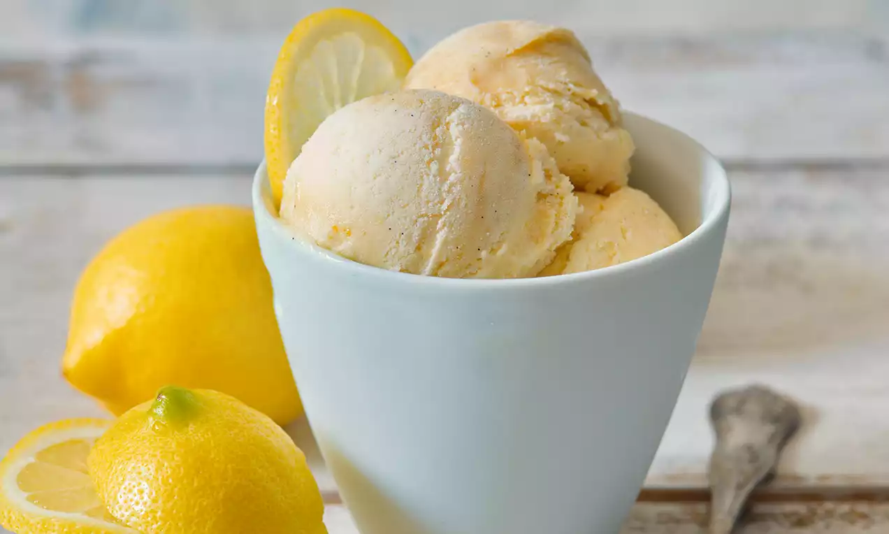 Vanilkovo-citronová zmrzlina světlé krémové barvy ve třech kopečcích v bílé misce, doplněná plátkem citronu a celými citrony na světlém pozadí