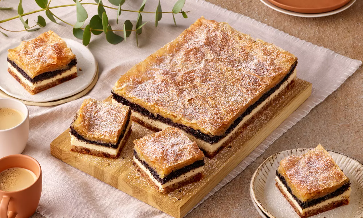 Gibanica mit goldbrauner, leicht knuspriger Teigdecke, geschichtet mit dunkler Mohn- und heller Quarkfüllung, auf einem Holzbrett serviert