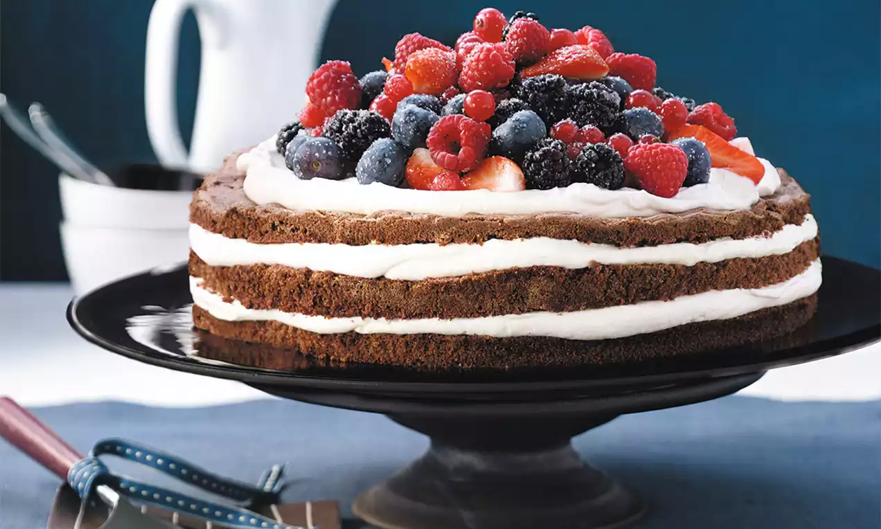 Vrstvený dort s mascarpone, hnědými korpusy, bílým krémem, posypaný čerstvými lesními plody na černém podnose