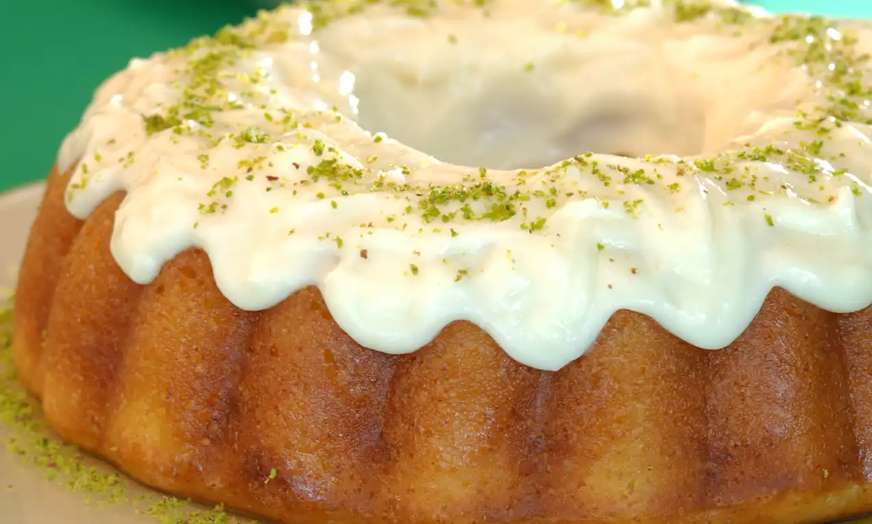 Kremalı beyaz sosla kaplanmış, altın rengi yuvarlak kek dilimli yapıda olup üzerine toz yeşil fıstık dökülmüş şekilde sunulmuş