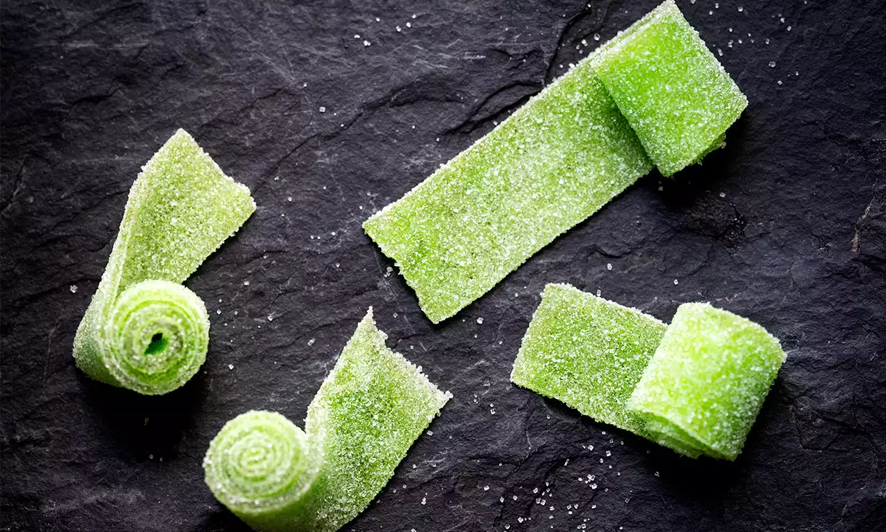 Lys grønne flate bånd med sukkerskimmer rullet og strukket utover på en ru, mørk steinoverflate