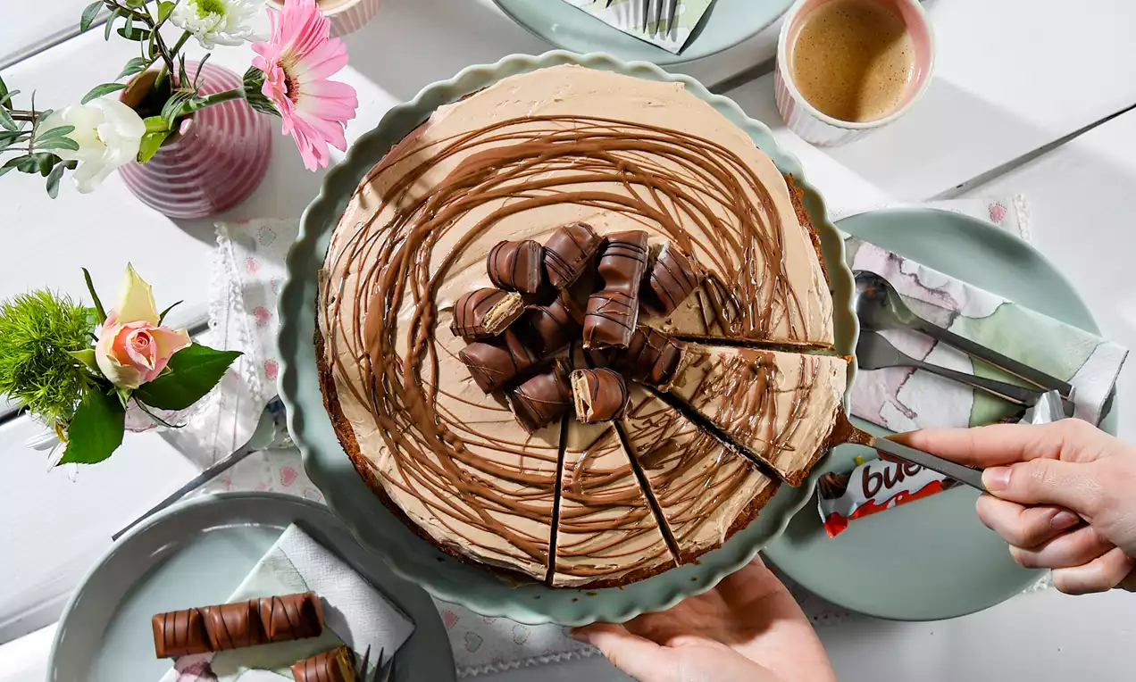 Kinder-Bueno-Torte mit cremiger hellbrauner Oberfläche, dekoriert mit Schokoladenstreifen und Bueno-Riegeln auf grünem Keramikteller