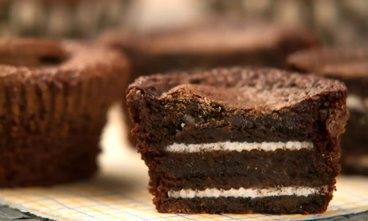 Brownie macio e escuro com camadas de bolacha recheada branca no centro sobre tecido xadrez amarelo e fundo desfocado