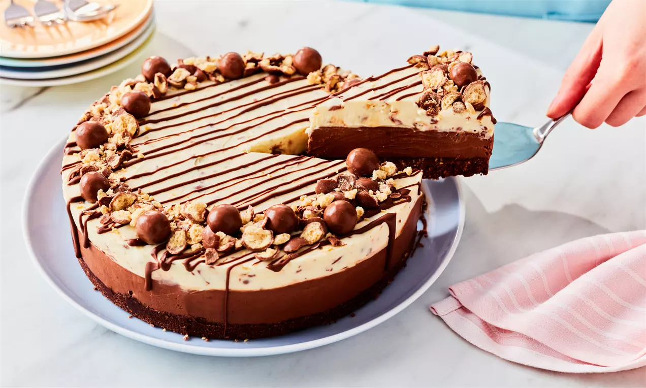 Round Malteser cheesecake with a dark biscuit base, creamy layers, chocolate drizzle, crushed Maltesers, and whole Maltesers on top