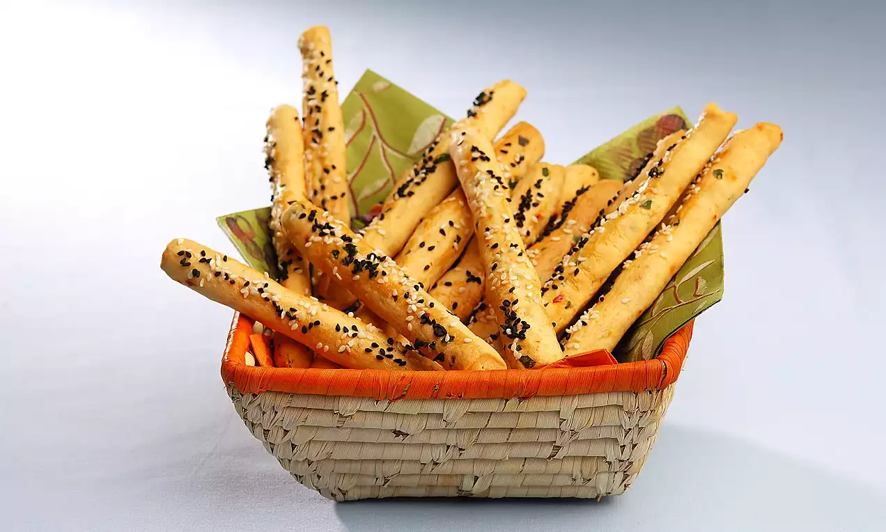 Uzun, altın rengi ince çubuklar üzerine siyah ve beyaz susam serpilmiş, örgü bir sepete renkli bir peçete üzerinde yerleştirilmiş