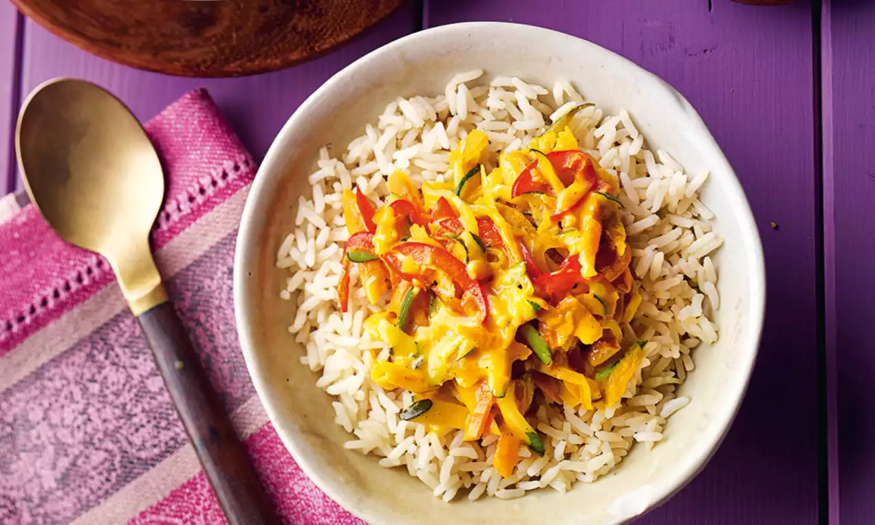Riso bianco soffice con crema giallo intenso e pezzi di verdure rosse e verdi disposti in una ciotola chiara su fondo viola