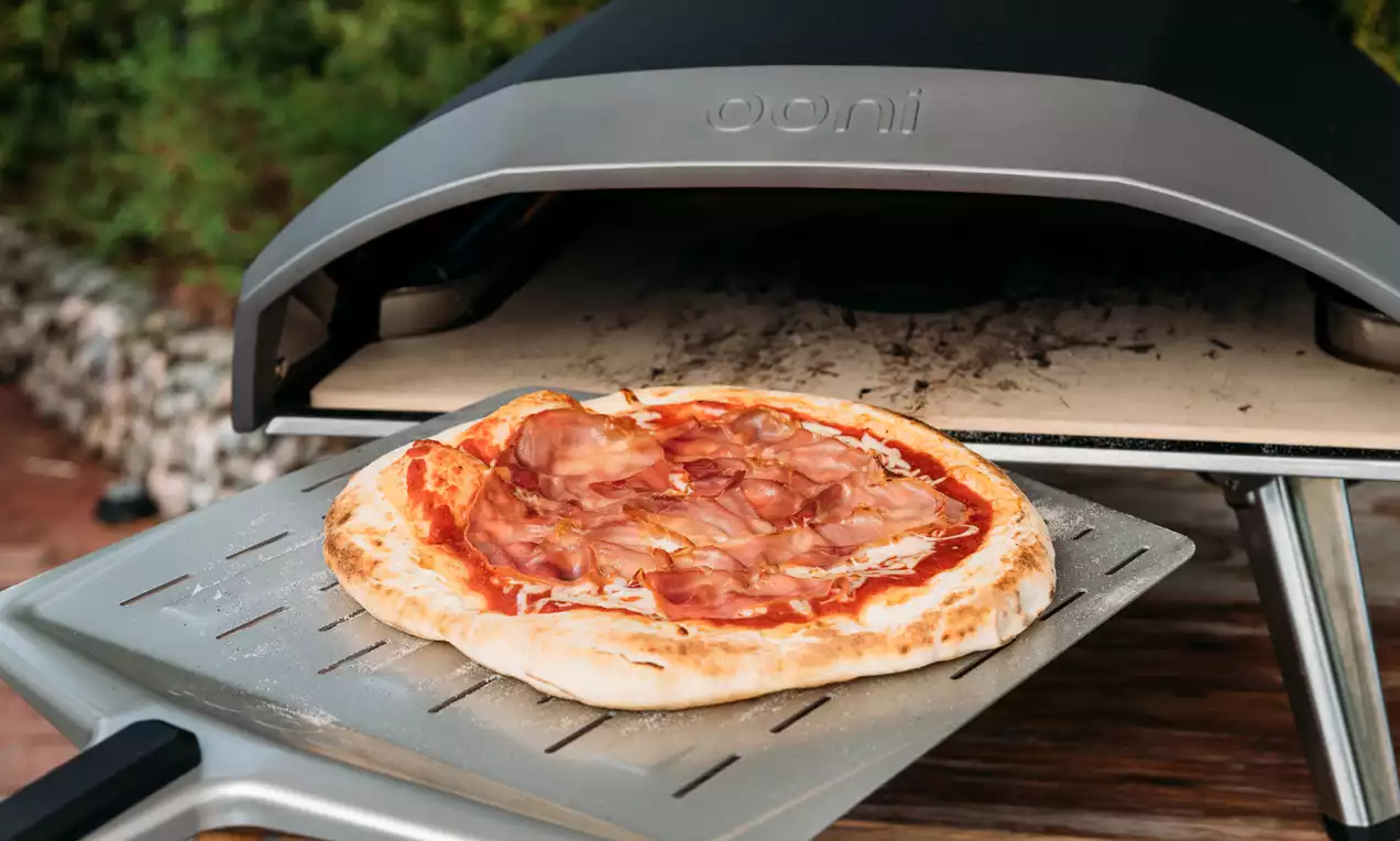 Vaaleanpunaisilla kinkkusiivuilla ja kirkkaanpunaisella tomaattikastikkeella täytetty pizza kultaisen kuoren ympäröimänä metallilastalla