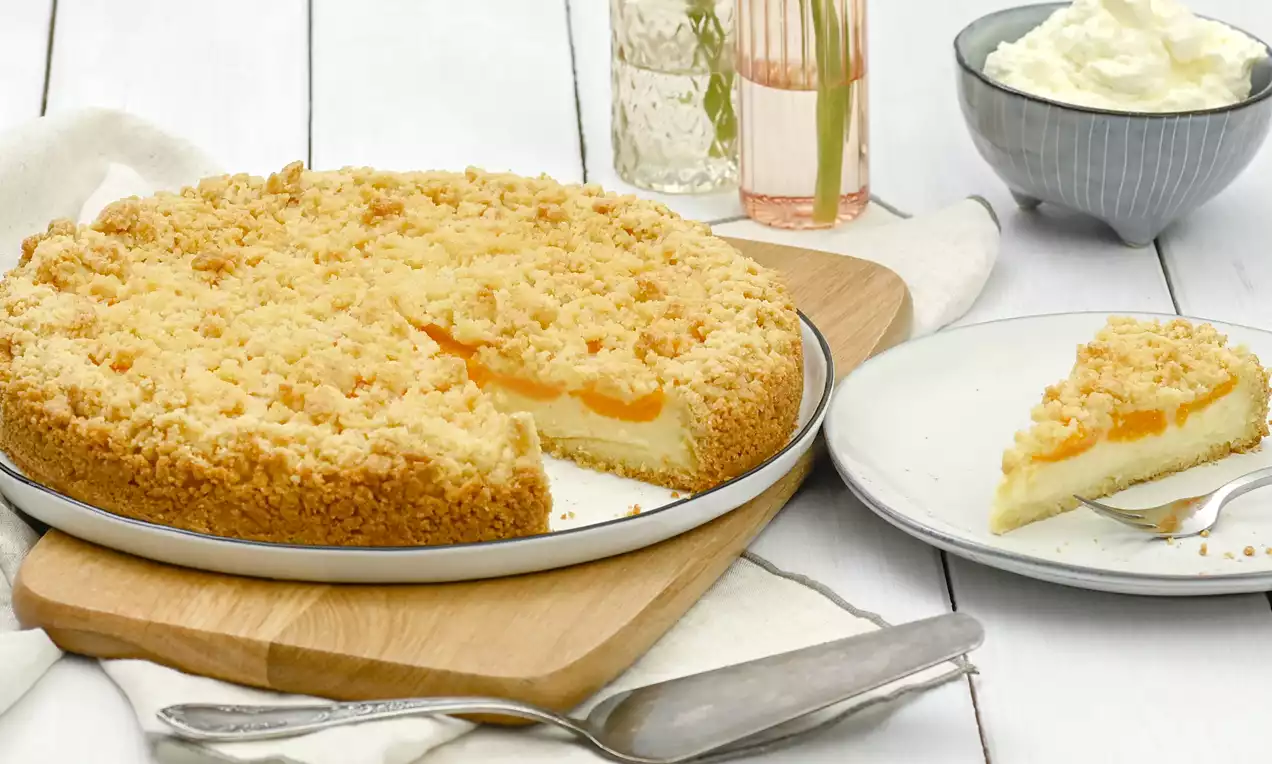 Goldbrauner Streuselkuchen mit cremiger Puddingfüllung und heller Teigbasis, auf einem Holzbrett mit Sahne und Teller im Hintergrund