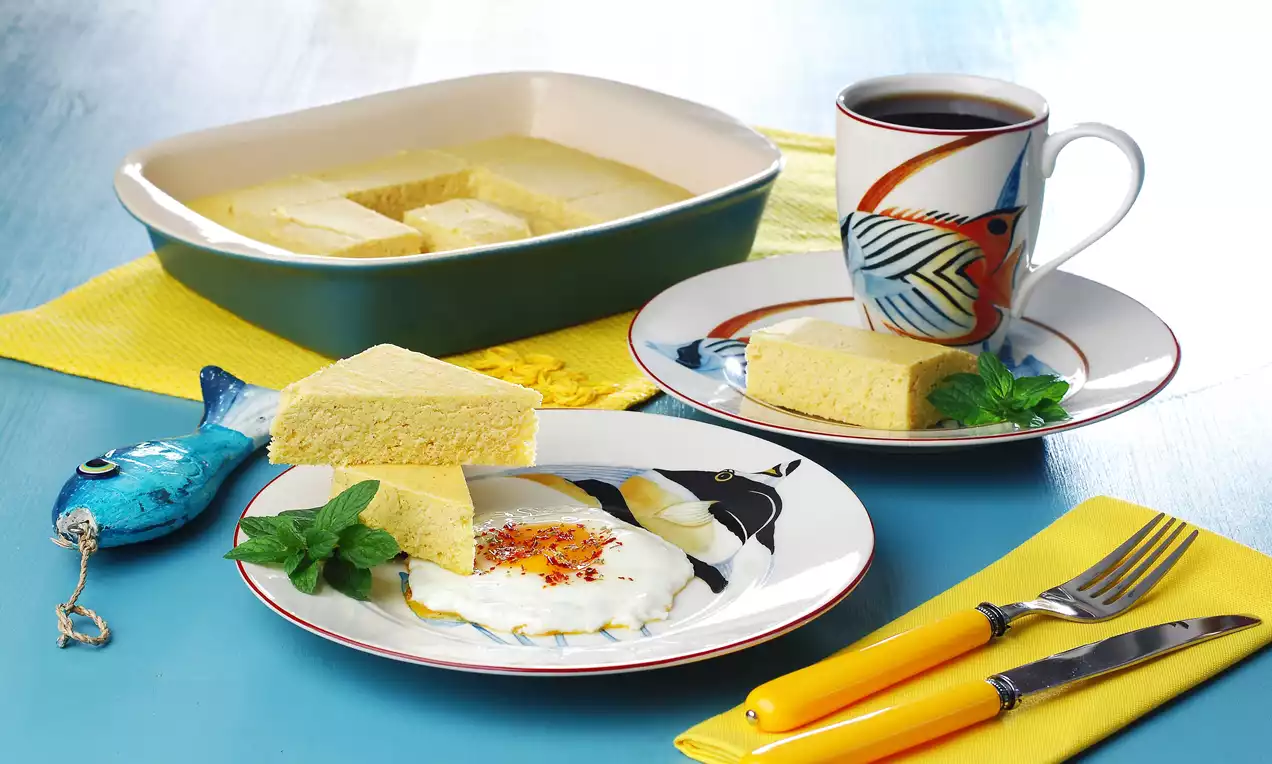 Altın sarısı mısır ekmeği parçaları, mavi desenli tabakta garnitürlü yumurta ile sunulmuş, yanında renkli fincanda kahve eşlik ediyor