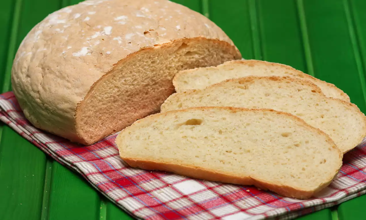 Yuvarlak beyaz ekmek, üstü hafif unlu, kırmızı kareli örtü üzerinde, üç dilim kesilmiş halde, yeşil çizgili zemin üzerinde