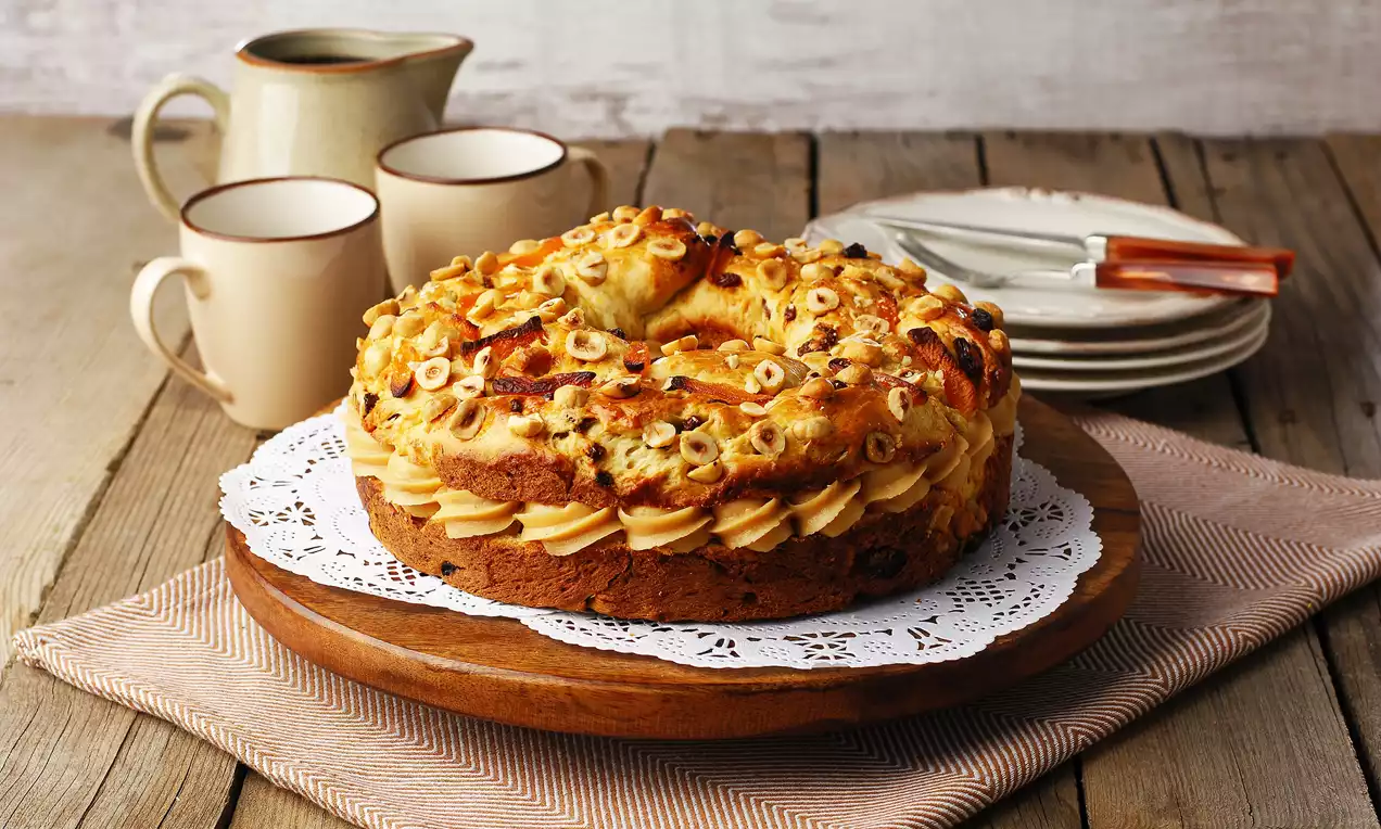 Fındık parçaları ve karamelli krema ile süslenmiş yuvarlak kek, dantel detaylı ahşap servis tabağında rustik bir ortamda sunulmuş