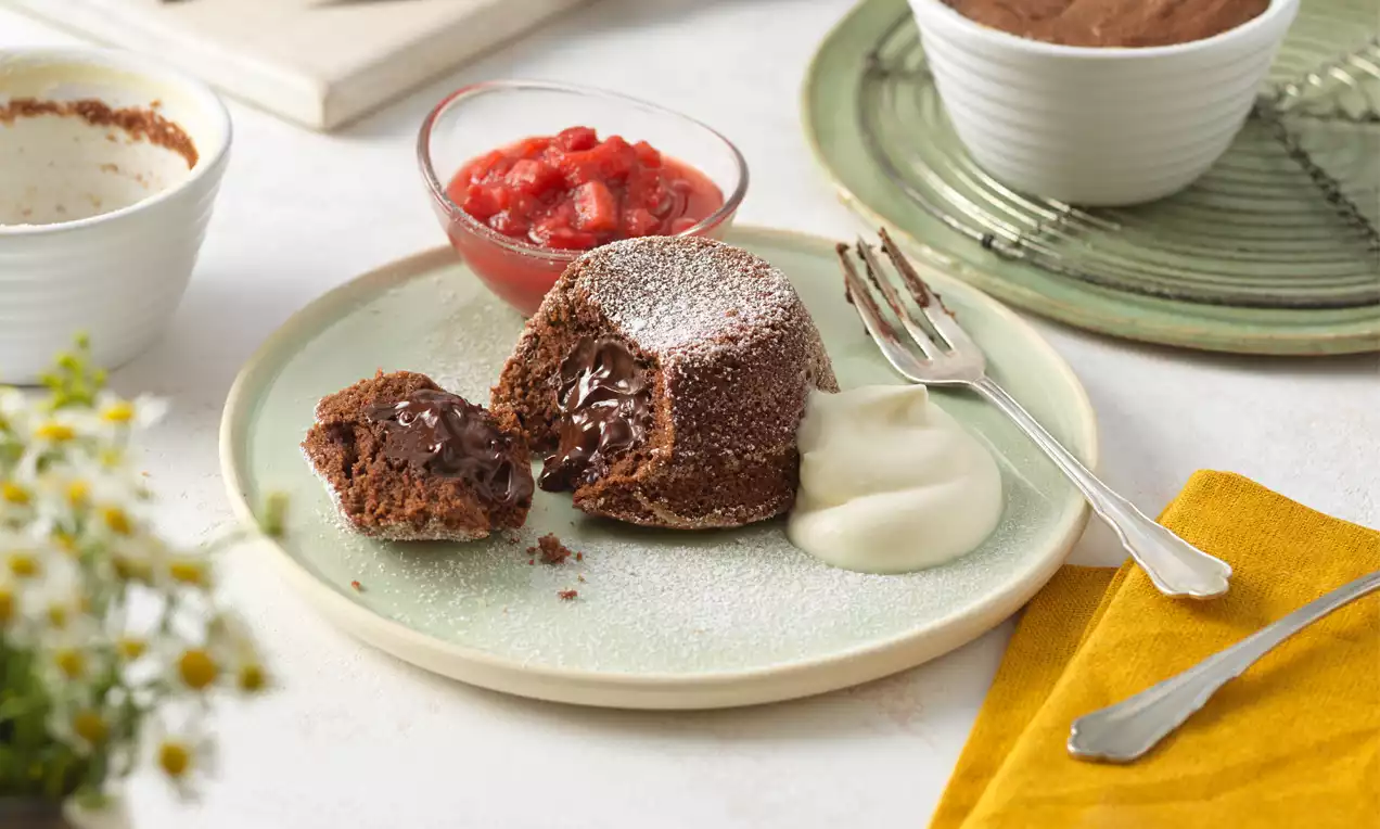 Schokoladen-Lava-Cake mit flüssigem Kern, bestäubt mit Puderzucker, serviert mit Sahne und Erdbeerkompott auf einem grünen Teller