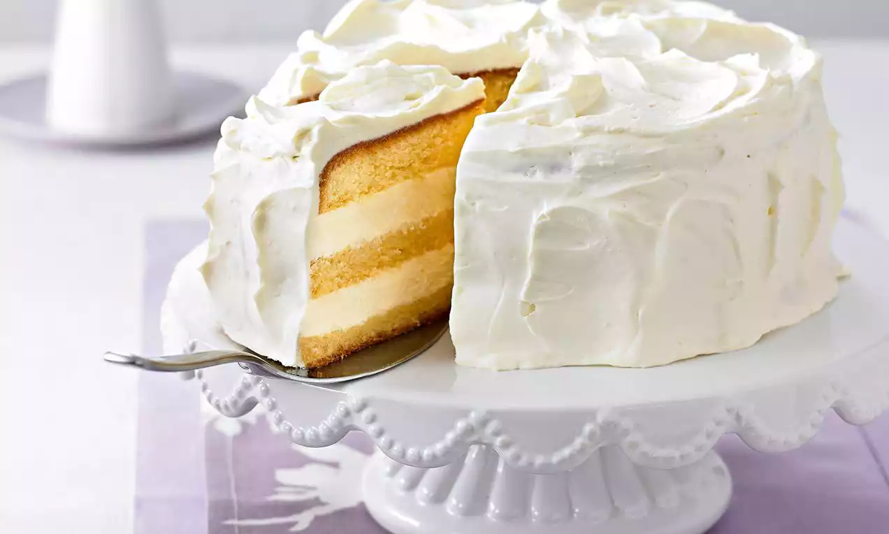 Helle Schichttorte mit lockeren gelben Böden und weißer Cremefüllung, mit weicher Sahne umhüllt auf einer verzierten weißen Tortenplatte