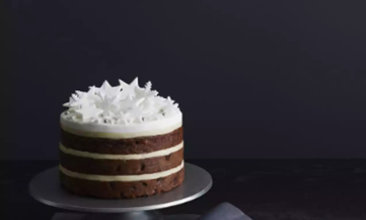 Layered Christmas cake with dark brown sponge, creamy white filling, and a delicate topping of white icing snowflakes on a grey stand