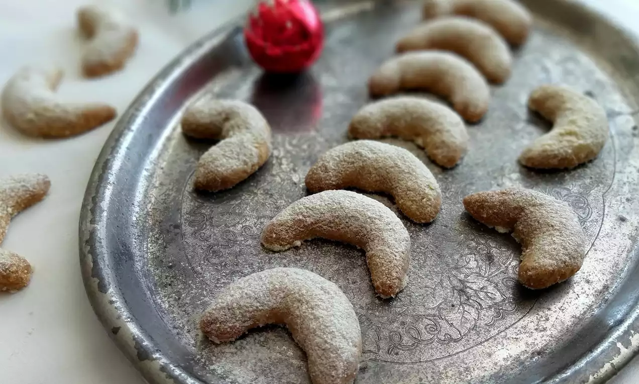 Špaldové rohlíčky jemne zlatohnedé, obalené v práškovom cukre, zakrivené do tvaru polmesiaca, usporiadané na striebornom podnose s vianočnou ozdobou