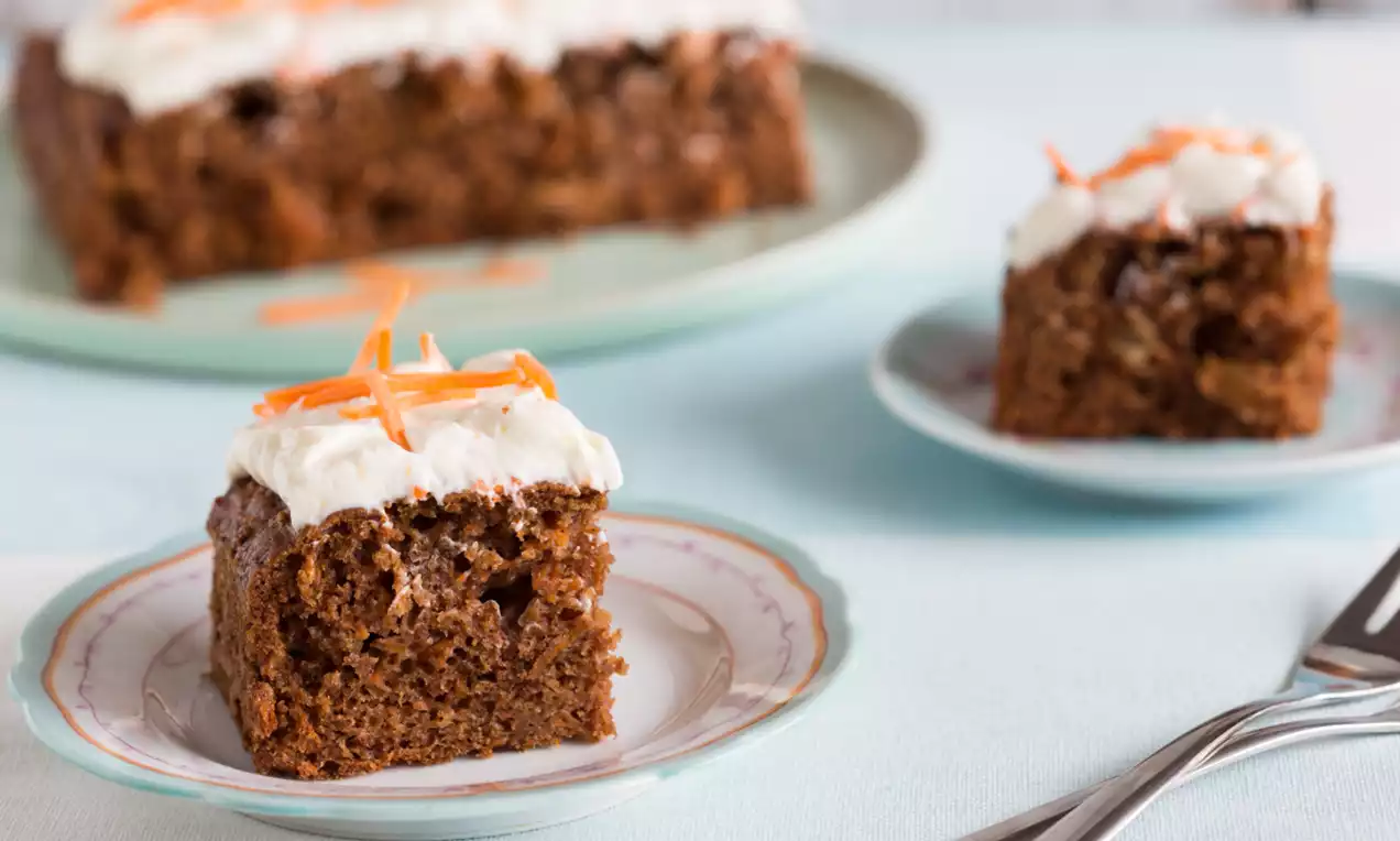 Carré moelleux couleur caramel foncé avec glaçage blanc crémeux et filaments de carottes orangés sur une assiette en porcelaine