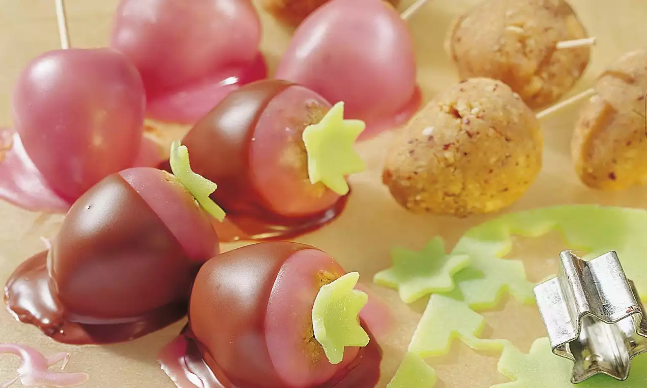 Runde Brombeeren mit glänzend rosa Glasur und Schokoladenschicht, verziert mit sternförmigen grünen Dekorelementen auf einem Holztisch