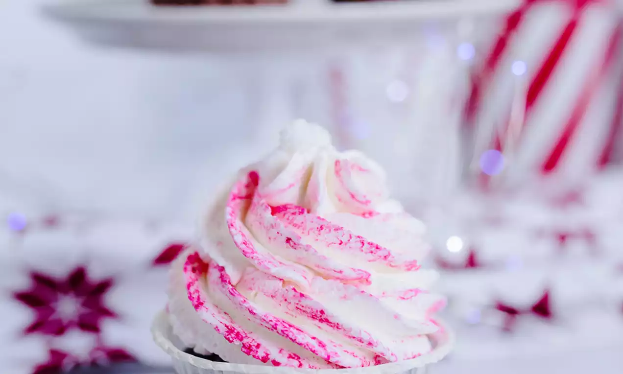 Čokoladni cupcake u papirnatom omotu, s bijelim i ružičastim kremastim swirl ukrasom na vrhu, postavljen na podložak uz božićne dekoracije