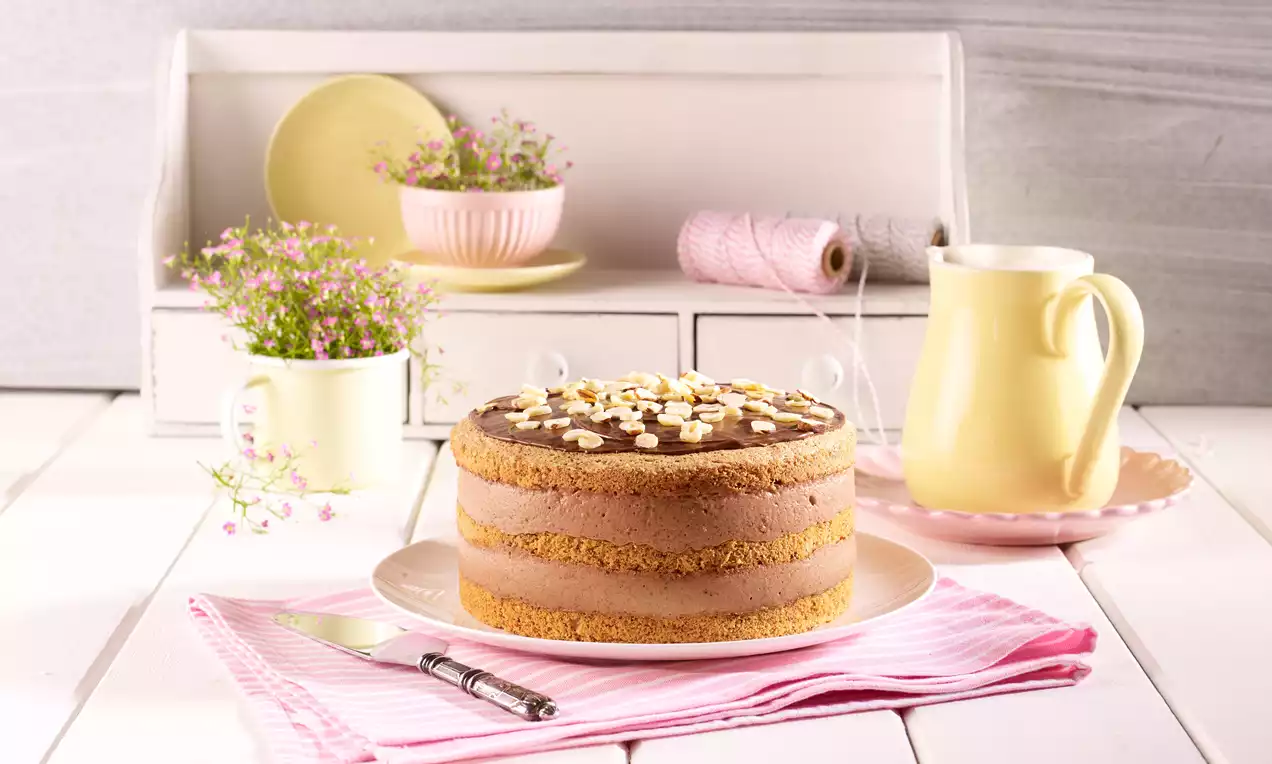 Kleine Nuss-Sahne-Torte auf weißer Tortenplatte mit saftigem Nussbiskuit, cremiger heller Sahnefüllung, gehobelten Nüssen und Schokoraspeln