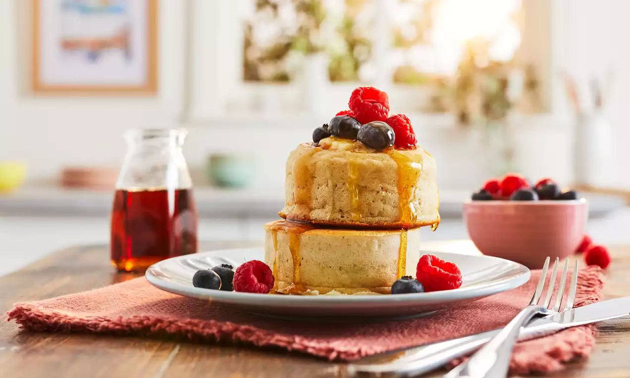 Debele, zlatnosmeđe japanske palačinke složene na tanjur, prelivene jantarskim sirupom, ukrašene svježim malinama i borovnicama