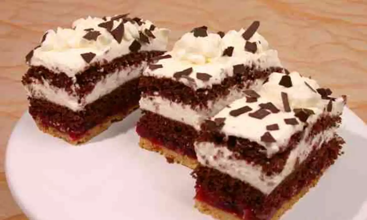 Herrenschnitten mit Schichten aus dunklem Schokoteig, heller Sahnecreme und Kirschfüllung, garniert mit Sahnetupfen und Schokoraspeln auf weißem Teller