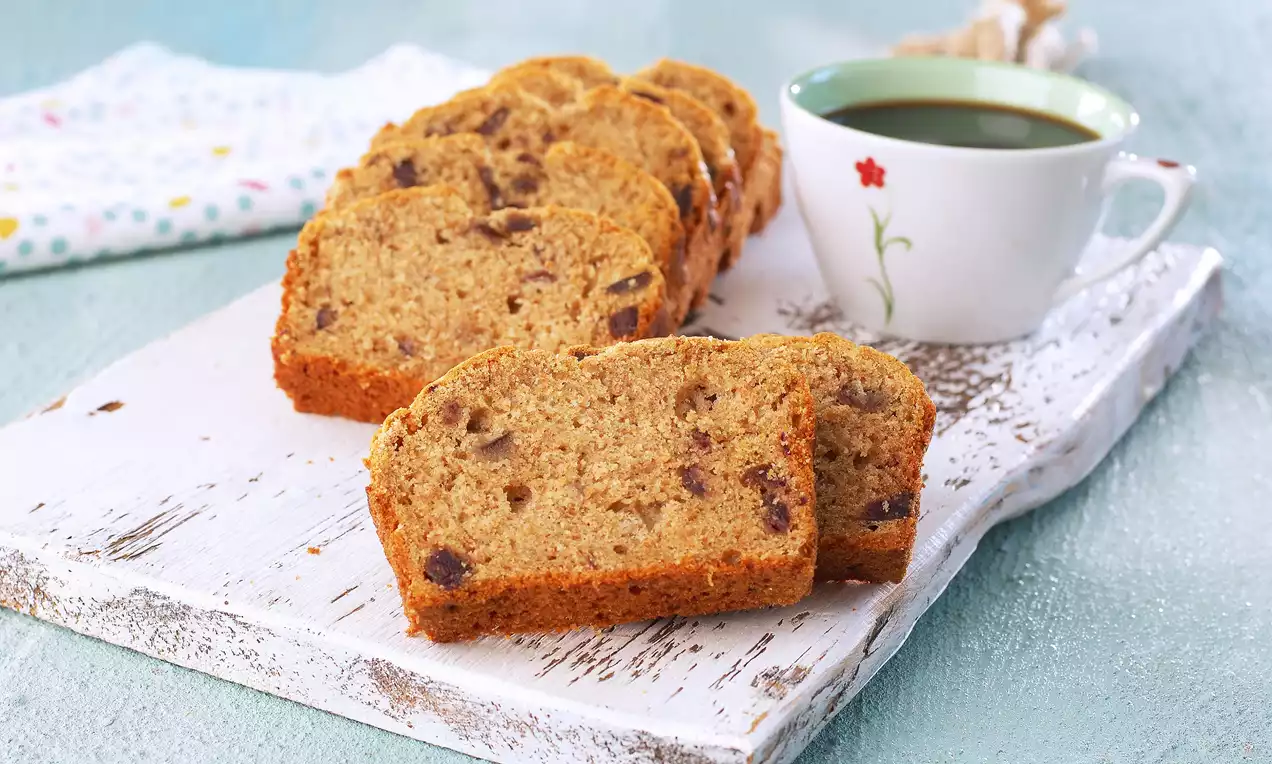 Tam buğday unuyla hazırlanan hafif kahverengi hurmalı kek dilimleri, rustik bir beyaz tahtada kahve fincanı eşliğinde sunulmuş