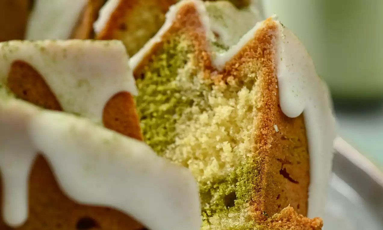 Plant based matcha-kakku vaaleanvihreillä ja kultaisilla kerroksilla, pehmeän valkoisella kuorrutteella, aseteltuna vaalealle lautaselle