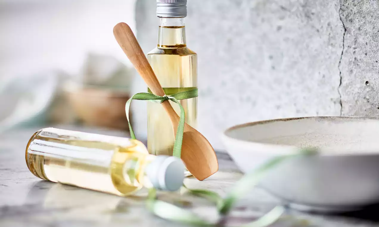 Bistrozlatni sirup u prozirnim, cilindričnim bočicama s metalnim čepovima, ukrašen zelenim vrpcama i drvenom žlicom na svijetlom stolu