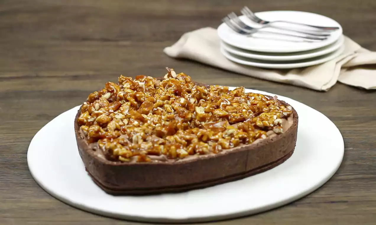 Torta em forma de coração com borda de massa crocante escura, recheio de nozes caramelizadas brilhantes sobre prato branco redondo