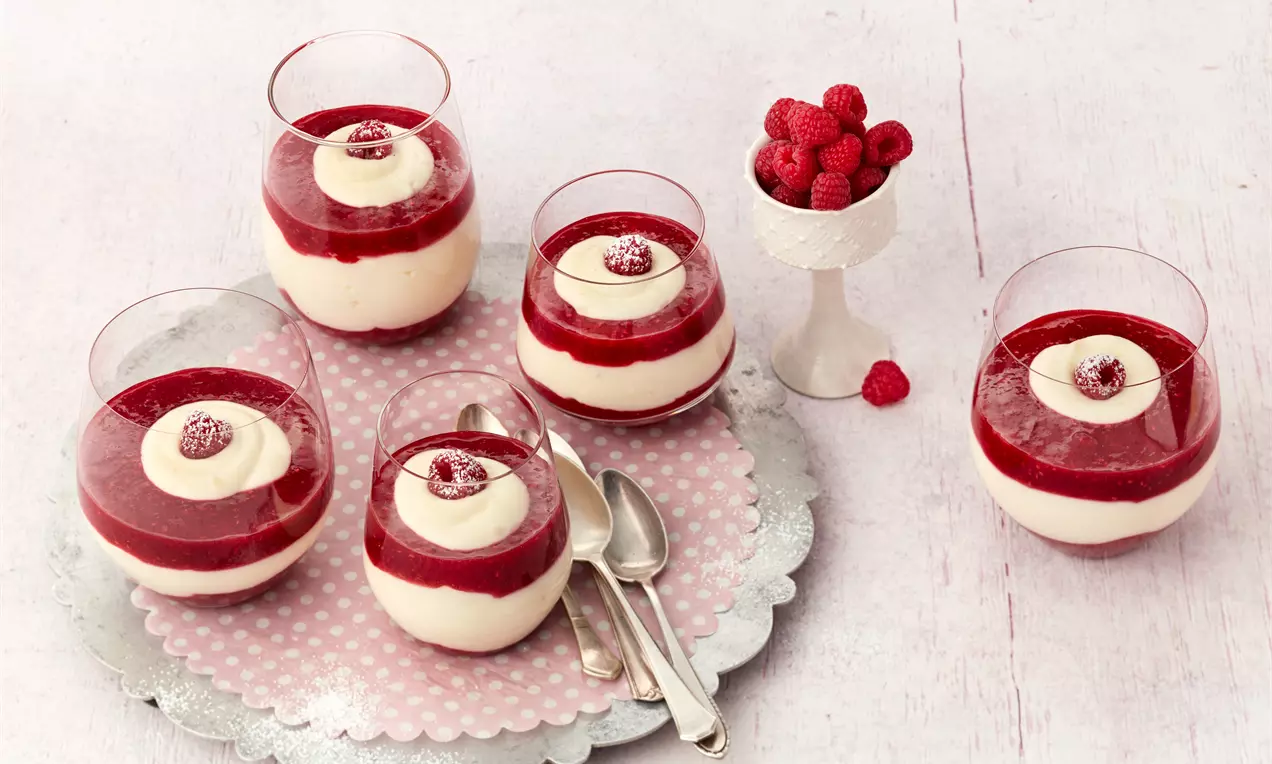 Gläser mit weißer Mascarponecreme und rotem Himbeerpüree, mit Sahnetupfen und Himbeeren, auf einem silbernen Tablett mit rosa Serviette