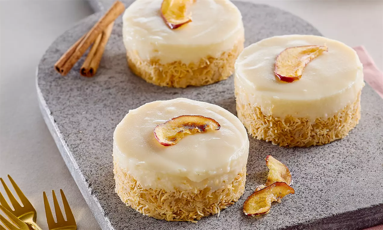 Yuvarlak formda beyaz tavukgöğsü kreması üzerinde ince elma dilimi, alt kısmı altın rengi kadayıf kaplı, gri mermer tabakta.