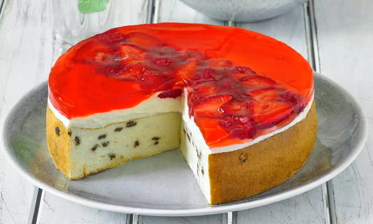 Jogurtová jahodová torta s červenou želatínou a plátkami jahôd na vrchu, krémovou bielou plnkou s hrozienkami na svetlosivom tanieri