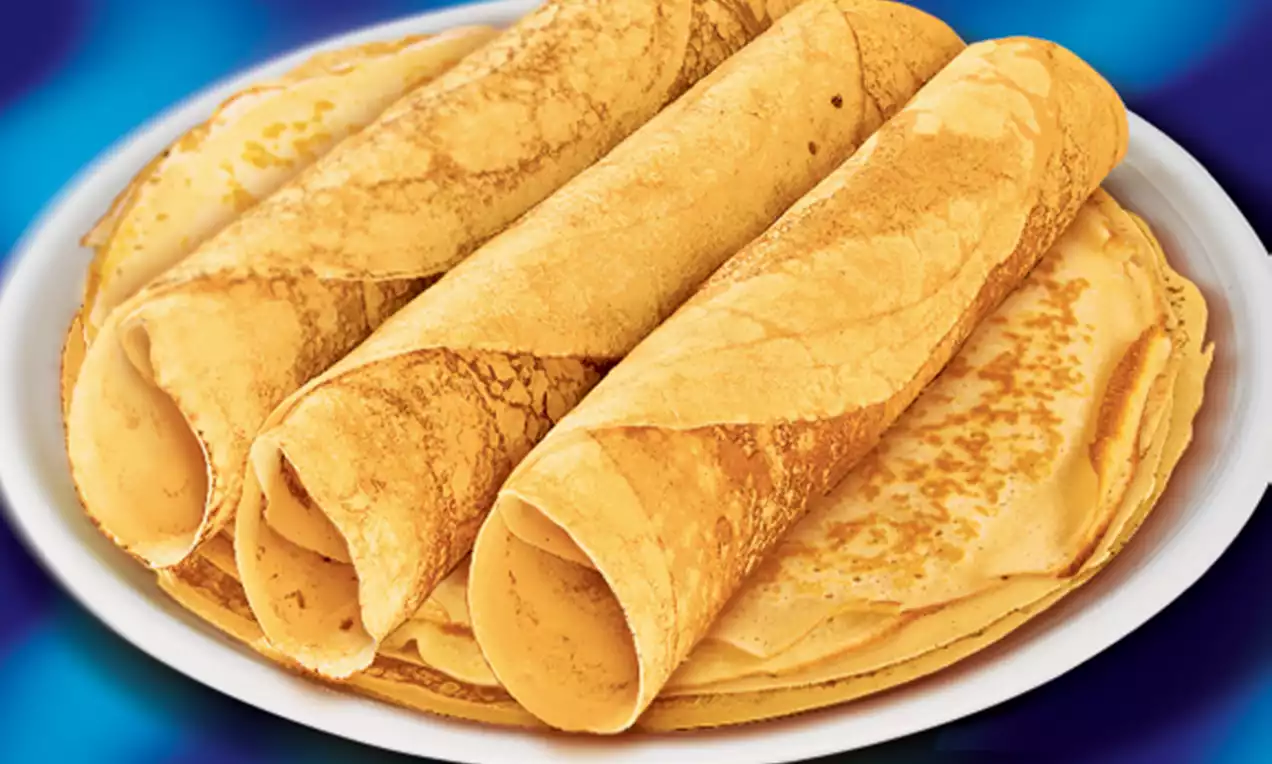 Crêpes fines et dorées roulées en cylindres légers, disposées sur une assiette blanche avec des nuances légèrement brunies