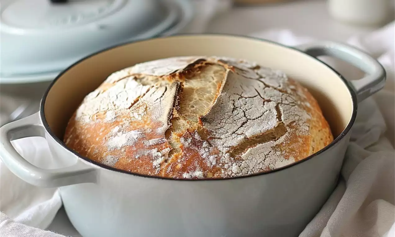 Pain à la croûte dorée et craquelée saupoudré de farine blanche, niché dans une cocotte bleu pâle sur un tissu blanc froissé