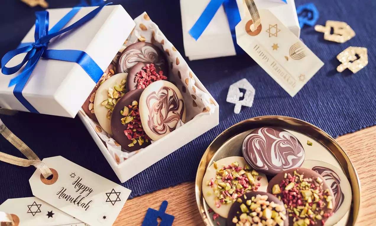 Round chocolate coins with marbled patterns, sprinkled with pistachios and dried fruit, arranged in a gold dish and white gift boxes