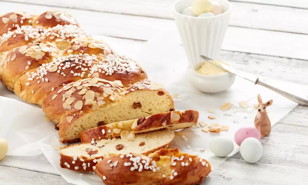 Osterzopf mit goldbraun glänzender Kruste, bestreut mit Hagelzucker und Mandeln, angeschnitten und dekoriert mit Ostereiern und kleinem Porzellan-Häschen