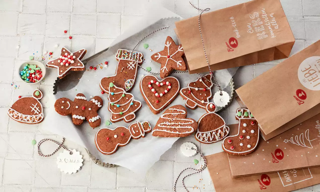 Bunte Lebkuchen in Weihnachtsformen, verziert mit farbigen Zuckerperlen und Zuckerguss, auf Pergamentpapier mit braunen Papiertüten arrangiert