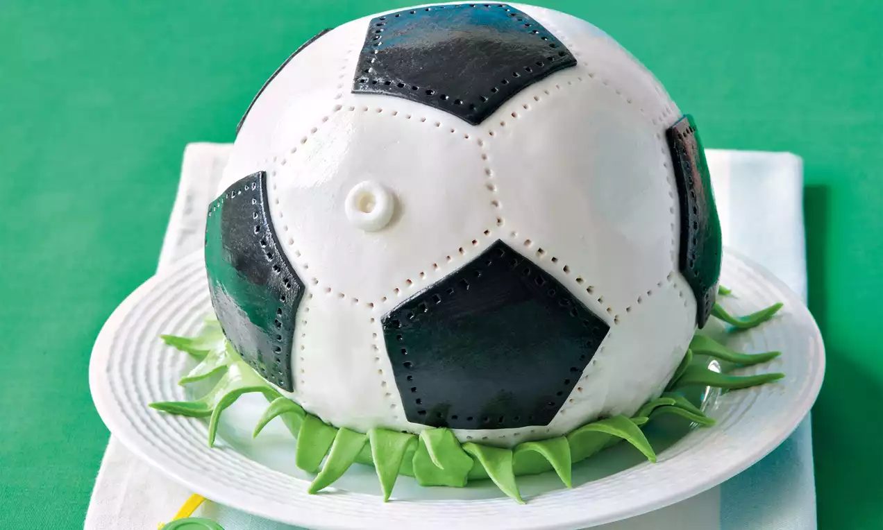 Futbalová lopta so šachovnicovým vzorom čiernych a bielych panelov, hladká a lesklá, položená na tanieri ozdobenom zelenými listami