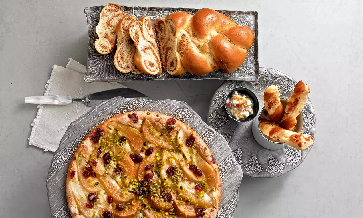 Hefeteig in unterschiedlich kreativen Formen, goldbraun gebacken, mit Pistazien und Cranberries, auf kunstvoll gemusterten Tellern angerichtet