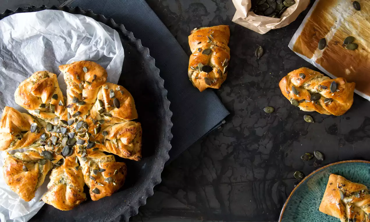 Goldbraune Ricottablume mit Kürbiskernen, blütenförmig gefaltet, auf einer schwarzen Platte mit weißem Backpapier drapiert