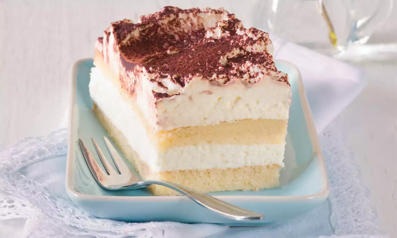 Jemné vrstvy piškót a mascarpone krému, posypané kakaovým práškom, servírované na bledomodrom tanieri so striebornou vidličkou.