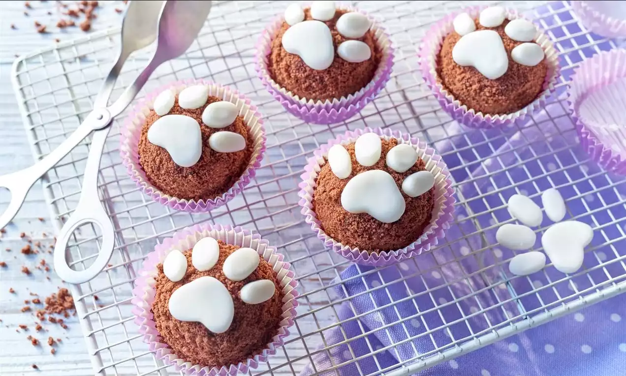 Miniatúrne krtkove torty v lila papierových košíčkoch, s hnedým čokoládovým povrchom a bielymi polevovými odtlačkami labiek na mriežke