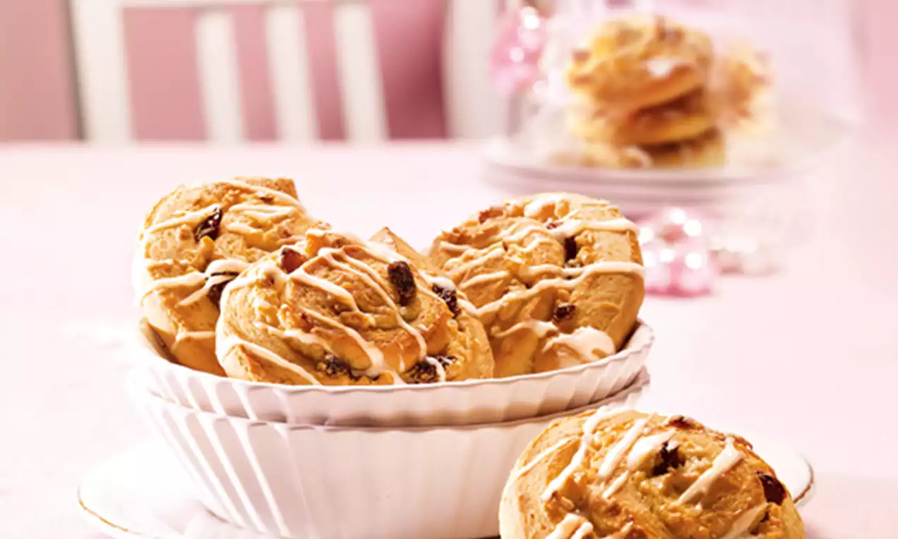 Marzipan-Nuss-Schnecken in hellem Teig, mit glasierter Oberfläche und Rosinen, arrangiert in einer weißen Schale auf rosa Tischdecke