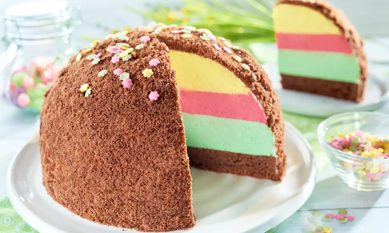 Kopiec z kakao o półkolistym kształcie z warstwami w kolorach zielonym, różowym i żółtym, posypany kolorową cukrową posypką na białym talerzu