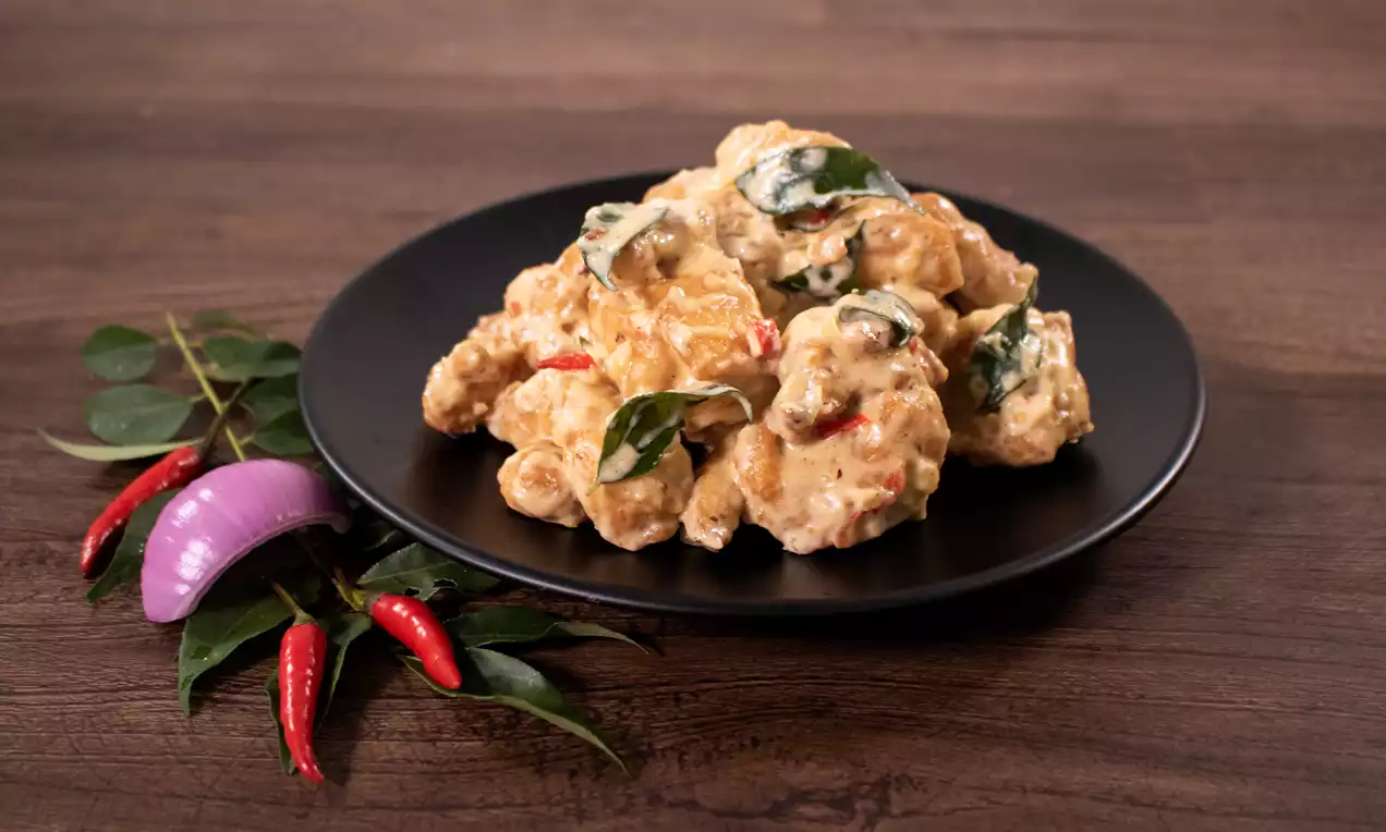 Creamy butter chicken in rich, golden-orange sauce dotted with curry leaves and red chilies on a black plate with onion and chili garnish