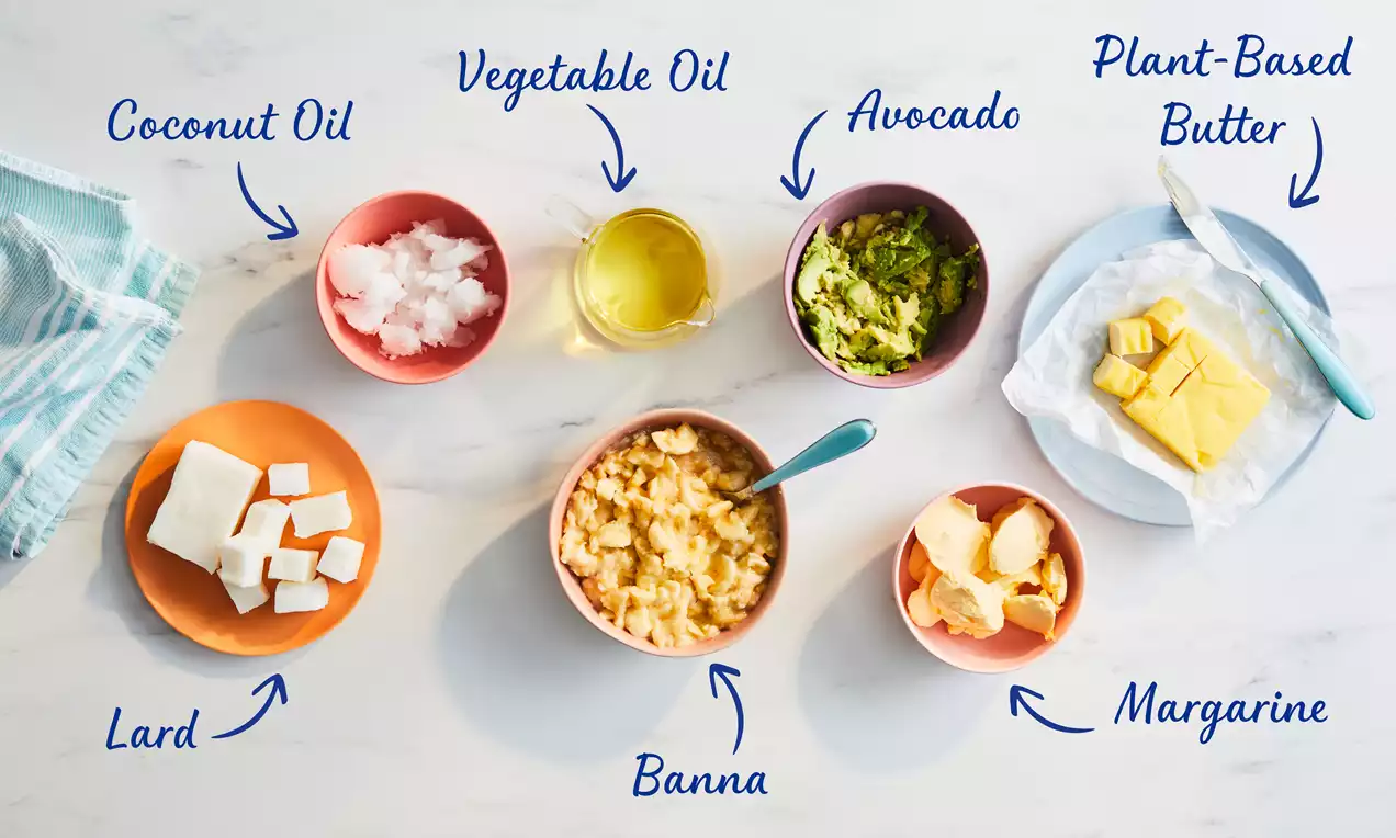 Six colorful bowls and a plate on a marble surface with butter alternatives, featuring cubes, mashed textures, oil, and avocado pieces