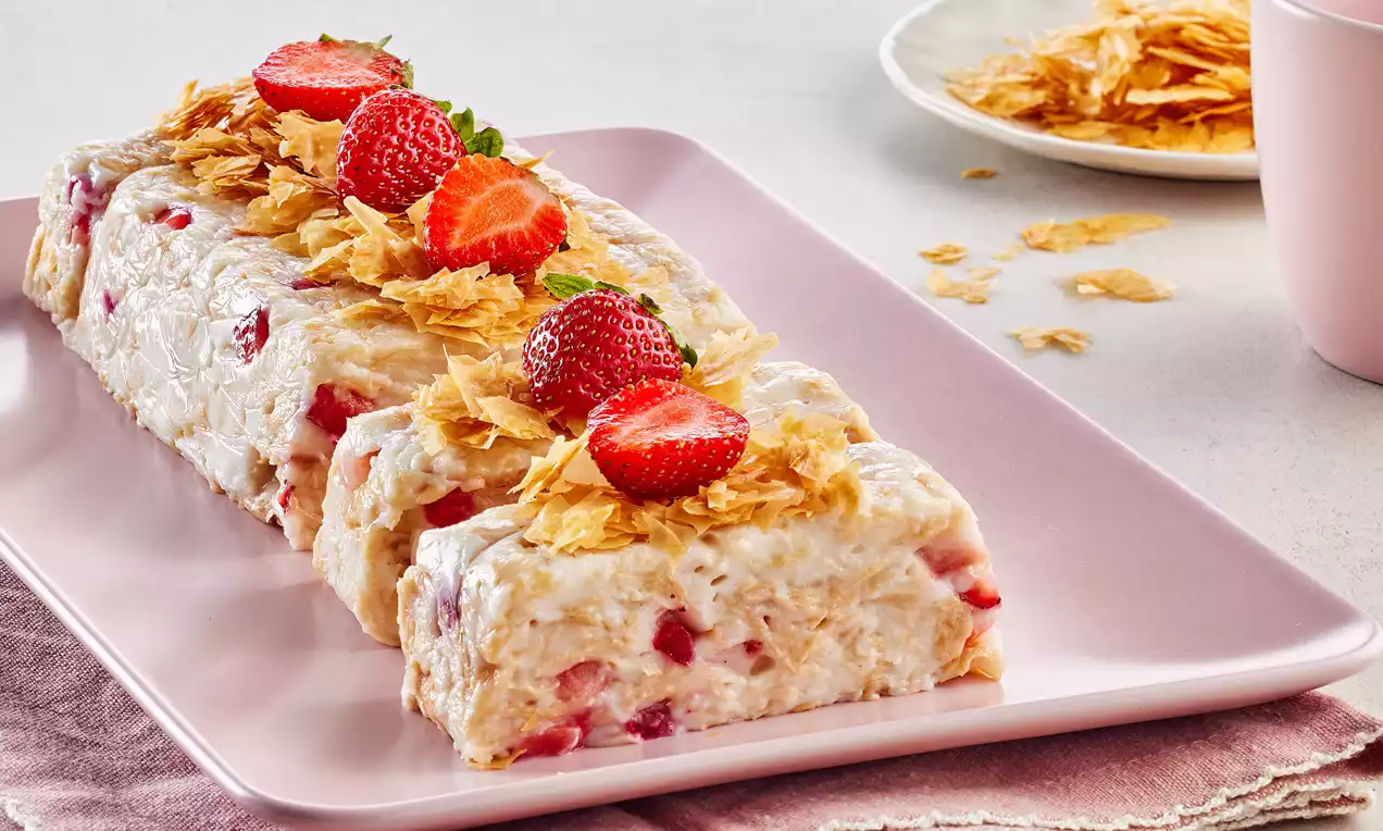 Pembe dikdörtgen tabakta, içinde çilek parçaları olan kremalı ve sakızlı tatlı, kıyılmış yufka ile kaplı ve çilek dilimleriyle süslenmiş