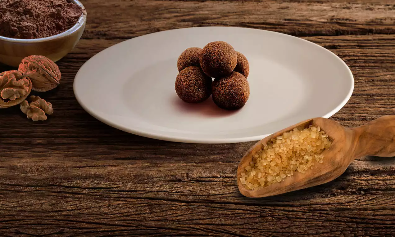 Hladké tmavohnedé guľôčky posypané kakaovým práškom usporiadané do pyramídy na bielom tanieri, obklopenom drevenými dekoráciami