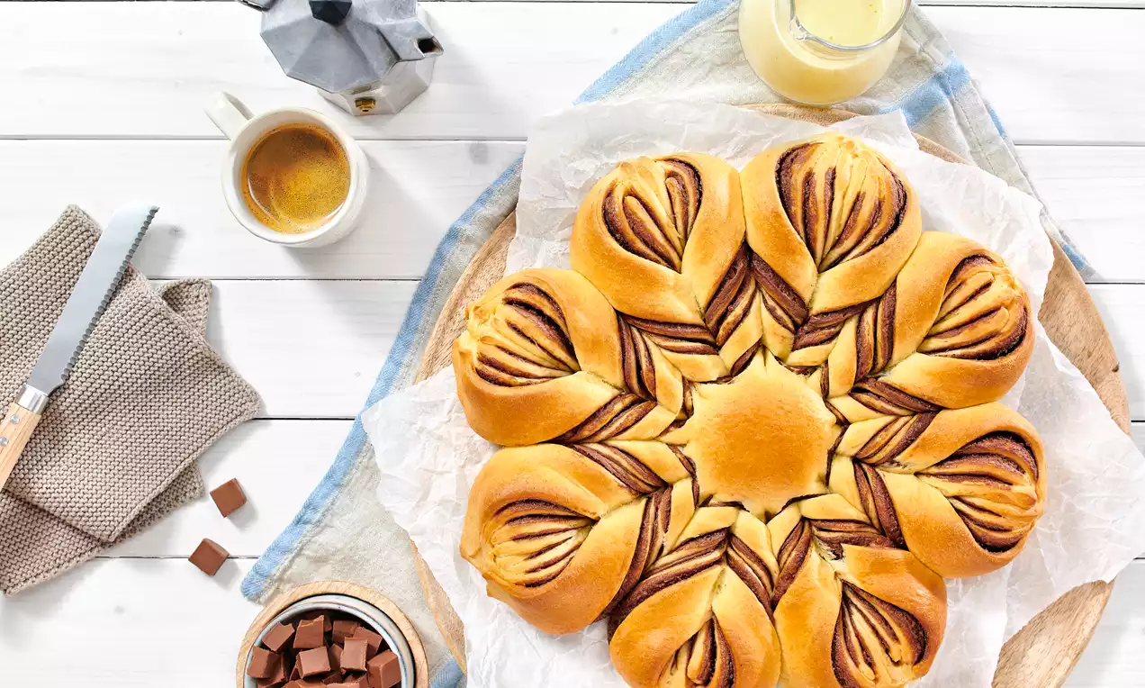 Nutella® Blume mit goldbraunen Teigblättern und glänzender Nutella-Nougatfüllung, leicht mit Puderzucker bestäubt auf weißem Teller