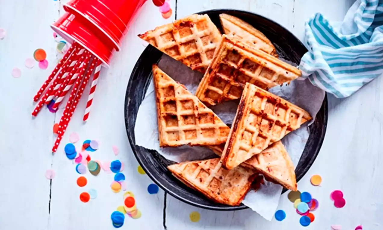 Golden triangular pizza waffles with a crisp texture and grill marks arranged on parchment in a black plate on a white table